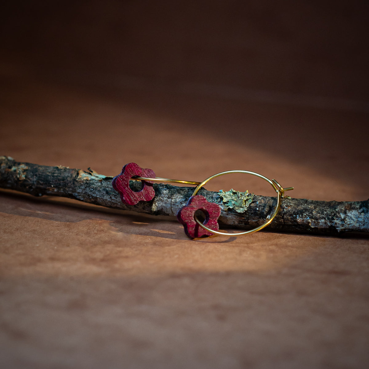 boucles d'oreilles créoles marguerite femme en bois d'amarante et acier doré, posées sur une branche, fabrication artisanale française, racines artisanat