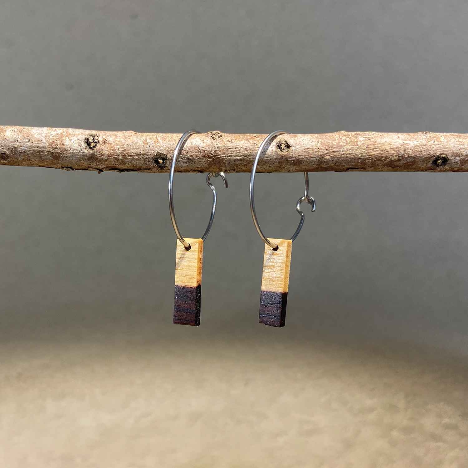 boucles d'oreilles créoles petite barre femme en aubier du bois de violette et acier argenté, suspendues à une branche, fabrication artisanale française, racines artisanat