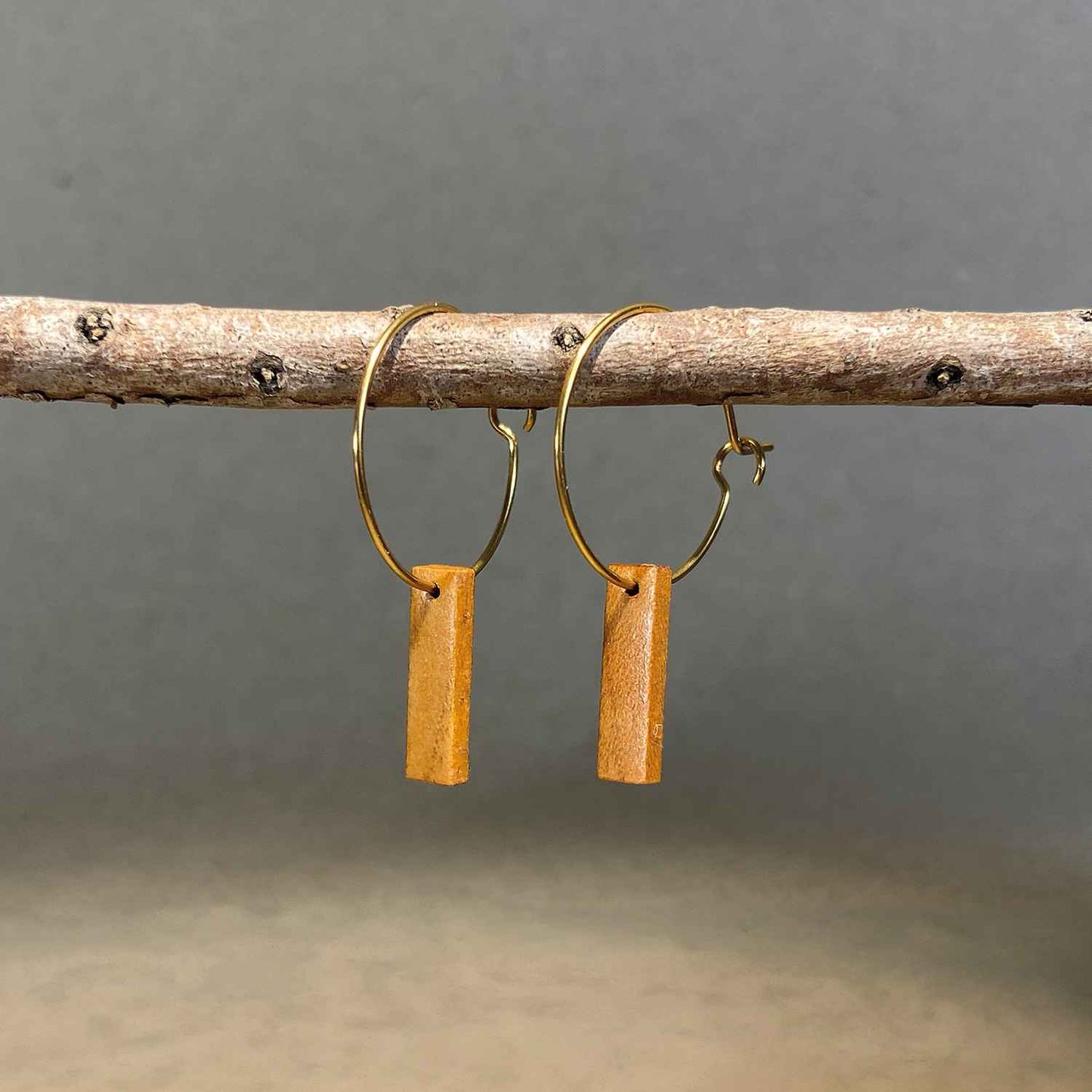 boucles d'oreilles créoles petite barre femme en bois de merisier et acier doré, suspendues à une branche, fabrication artisanale française, racines artisanat