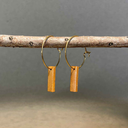 boucles d'oreilles créoles petite barre femme en bois de merisier et acier doré, suspendues à une branche, fabrication artisanale française, racines artisanat