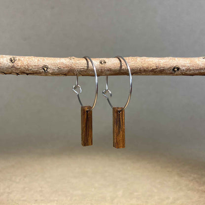 boucles d'oreilles créoles petite barre femme en bois de noyer et acier argenté, suspendues à une branche, fabrication artisanale française, racines artisanat