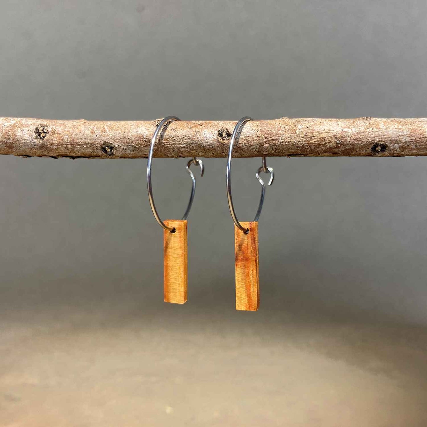 boucles d'oreilles créoles petite barre femme en bois de rose et acier argenté, suspendues à une branche, fabrication artisanale française, racines artisanat